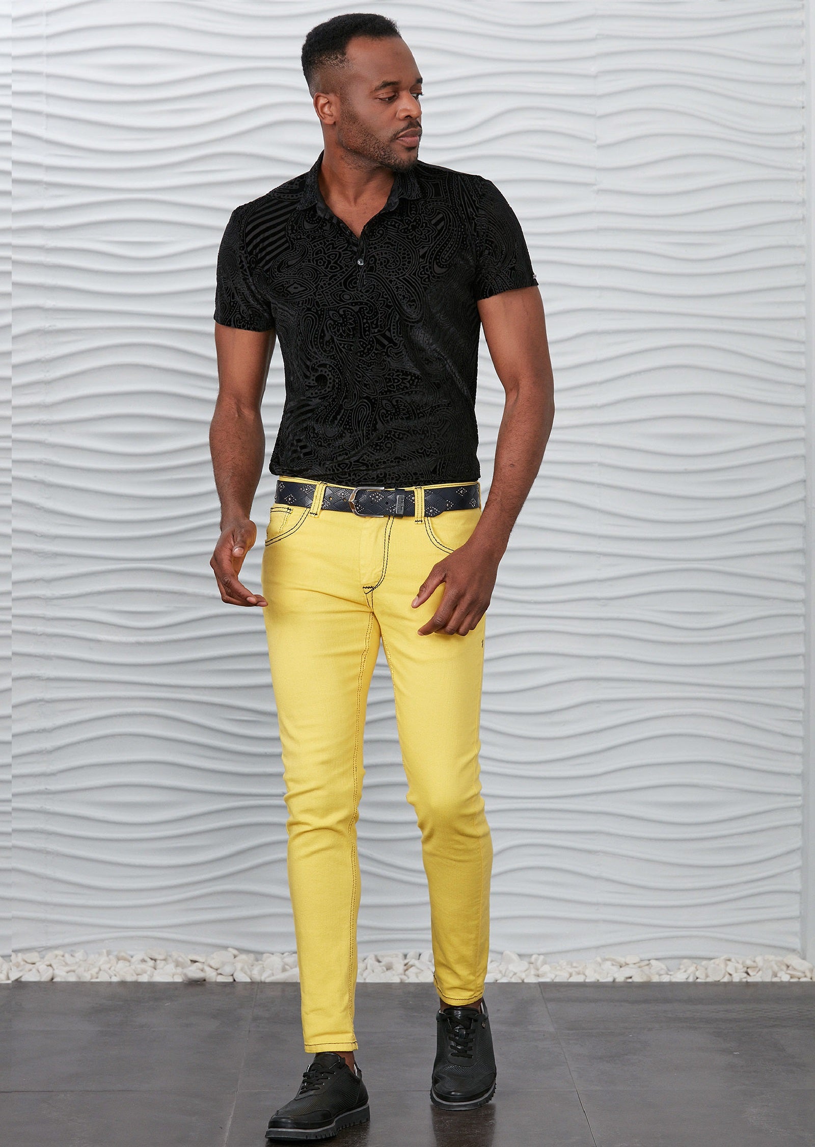 Dressing in a light yellow shirt gray pants and black shoes a young black  guy is standing by a glass wall and against a metal structure on the corn  Stock Photo 